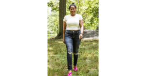 College Student wearing white shirt, jeans, and pink shoes walking outside smiling